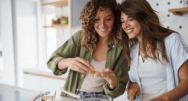 Young women laughing together while preparing a healthy meal in a modern kitchen, connecting and being present without distractions